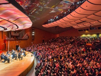 A chamber orchestra performs for an audience in a large auditorium.