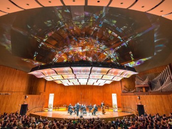 A chamber orchestra performs in a large auditorium.