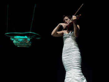 A violinist performs next to a hanging scupture.